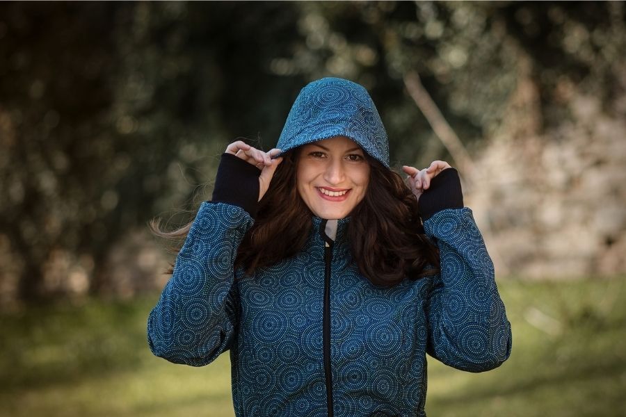 Porträt einer lachenden Frau, die die Kapuze einer blauen Jacke mit Mandalamuster hält